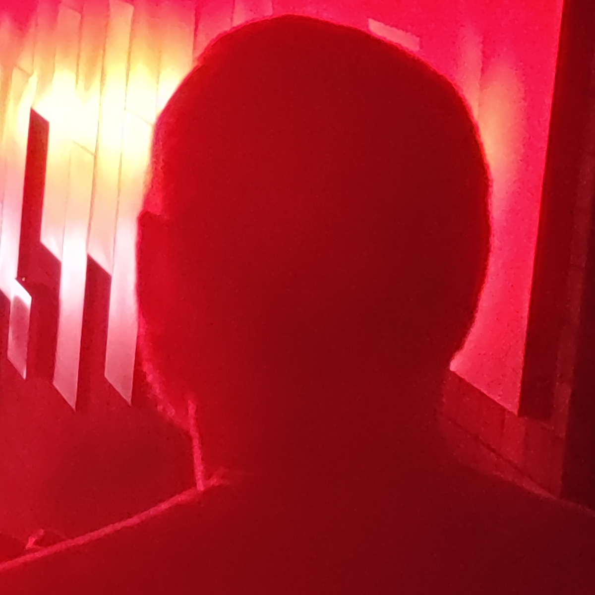 Dark, faceless silhouette of a person's head and shoulders against a deep red background