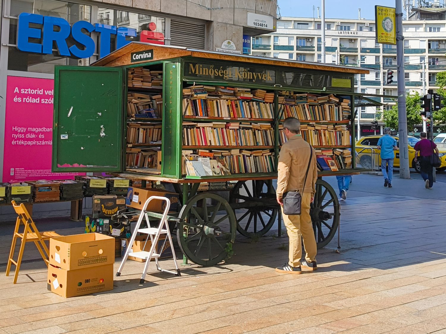 A man browsing alone at an outdoor second-hand book stall as people pass by on the street